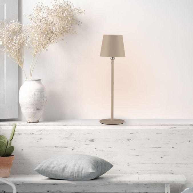 Lampe à poser beige en situation sur rebord, vase de fleurs séchées et coussin clair.