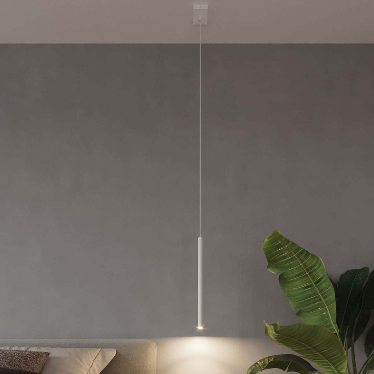 Mise en ambiance d'un pendant cylindrique blanc éclairant un mur gris près d'une plante.
