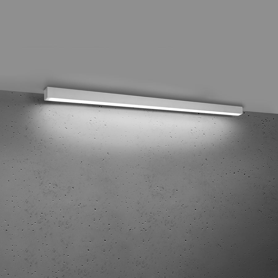 Luminaire allumé diffusant une lumière blanche froide sur le mur gris.