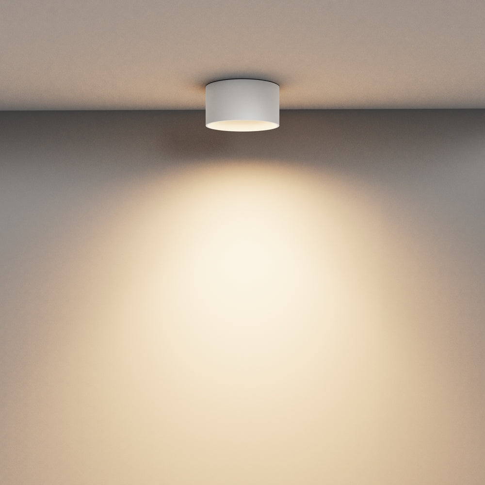 Mise en ambiance : luminaire blanc au plafond diffusant un halo chaud sur le mur