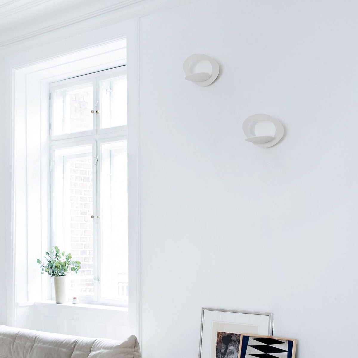 Deux appliques blanches fixées au mur près d’une fenêtre, ambiance intérieure épurée.