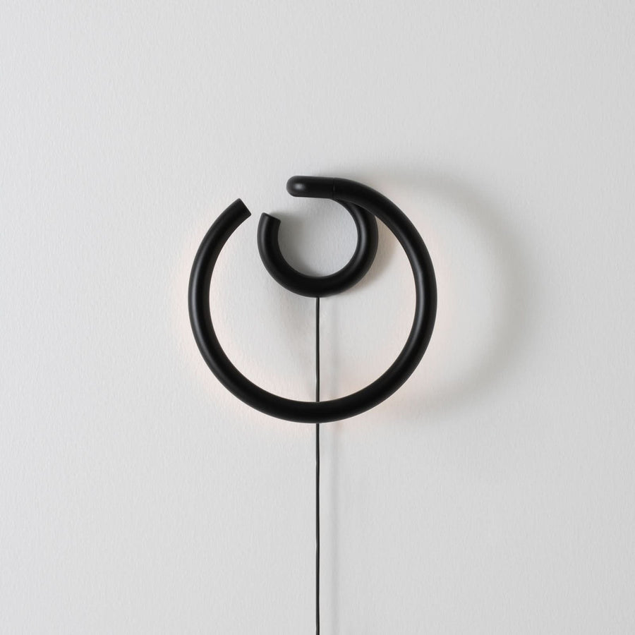 Silhouette noire de l’applique éteinte sur un mur blanc, câble apparent.