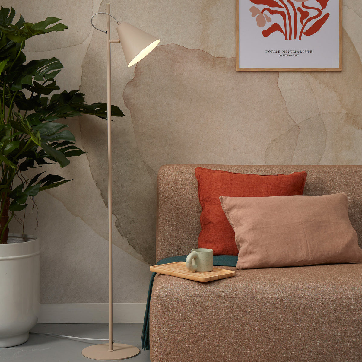 Mise en ambiance du lampadaire éclairant un canapé avec plante et tasse.