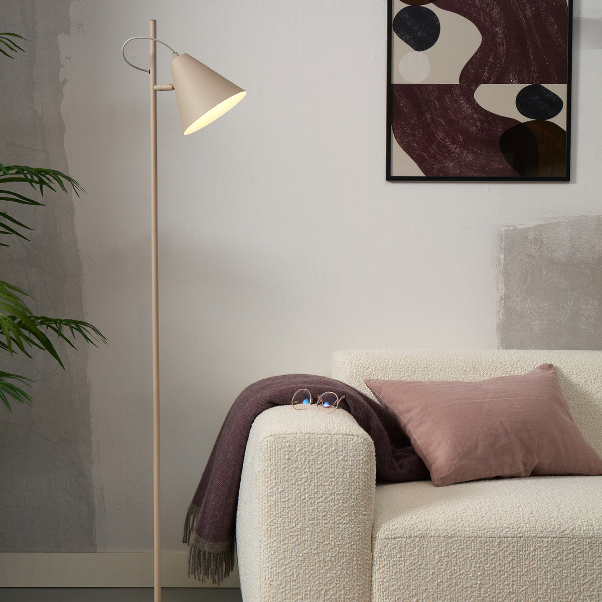 Lampadaire beige placé près d'un canapé blanc avec coussins et tableau mural.