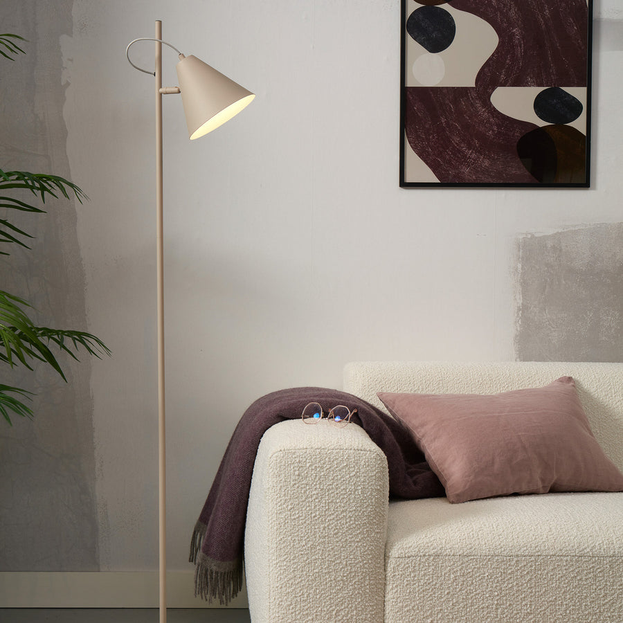 Lampadaire beige placé près d'un canapé blanc avec coussins et tableau mural.