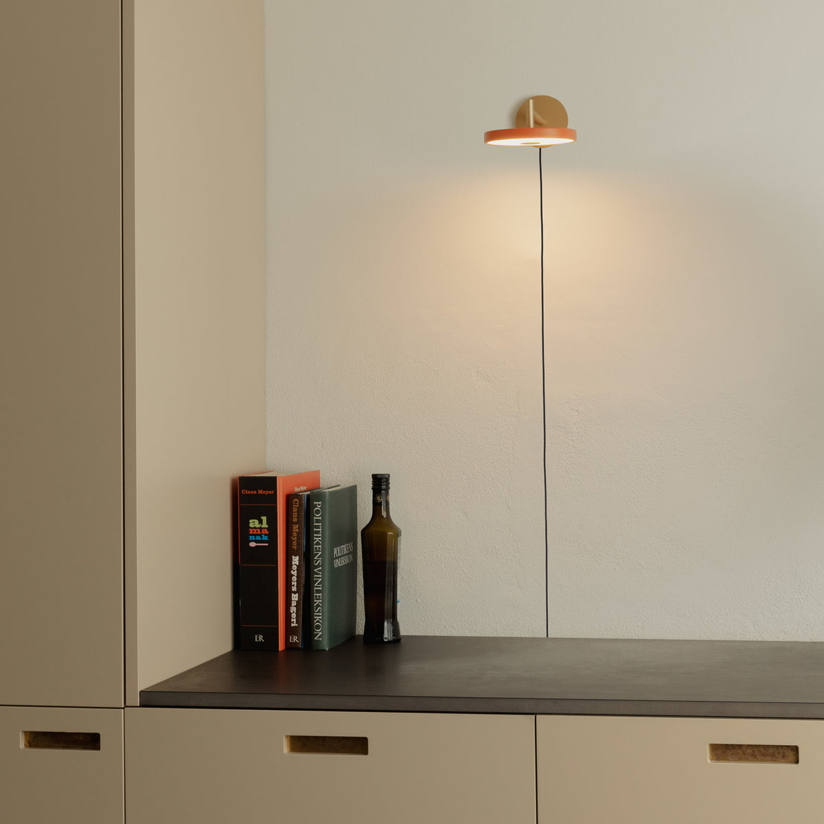 Mise en ambiance de l'applique murale au-dessus d'un meuble bas avec livres et bouteille.