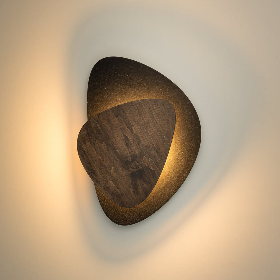 Applique murale allumée sur mur blanc, halo lumineux derrière la partie en bois.
