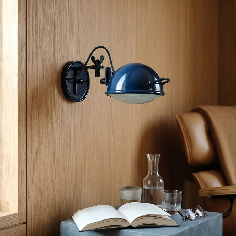 Applique murale bleue au-dessus d’un livre ouvert, d’une carafe et de lunettes.