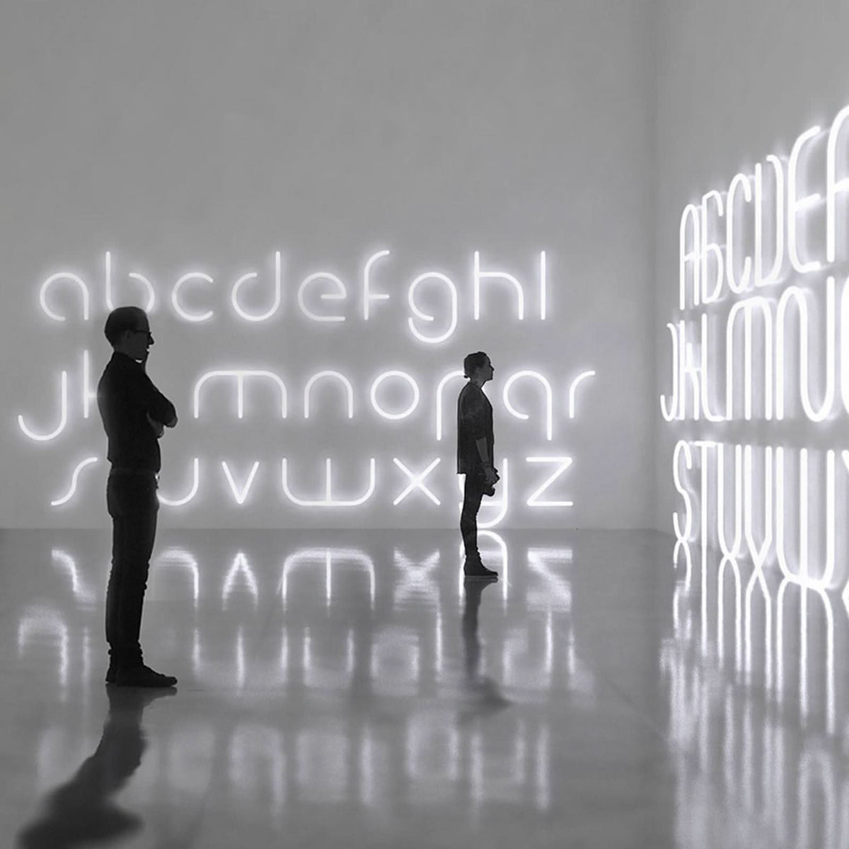 Vue d’ambiance avec grandes lettres lumineuses murales et deux silhouettes dans une salle.