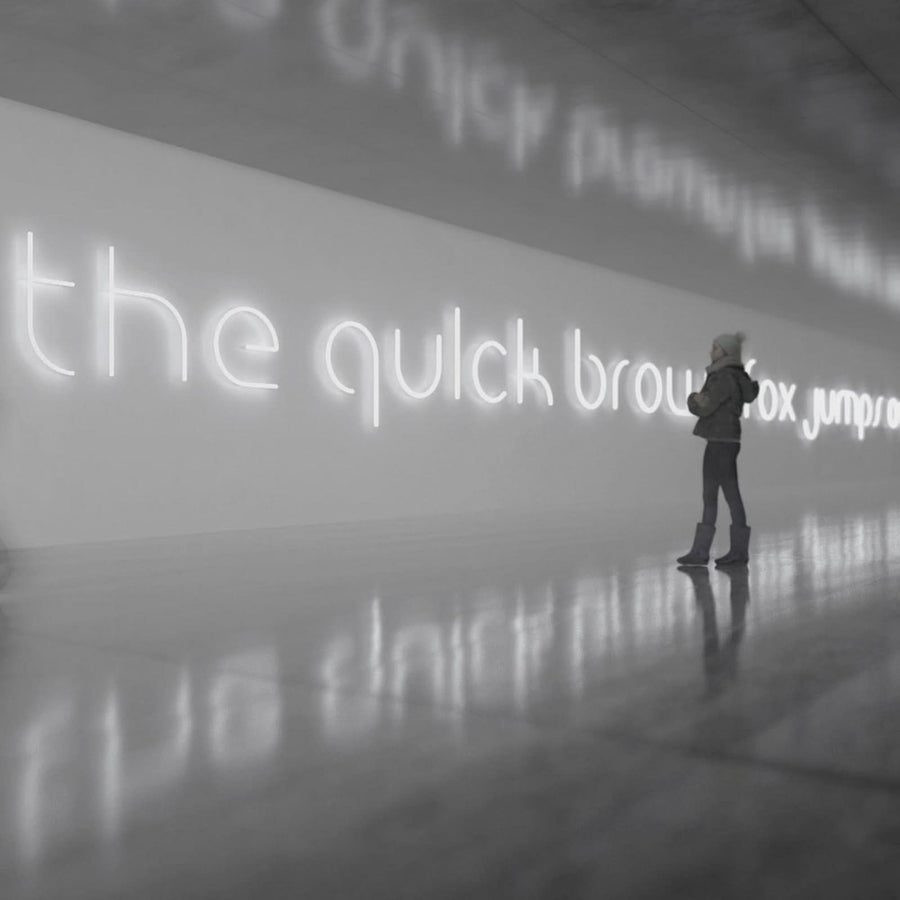 Vue en perspective d'une phrase lumineuse blanche sur un mur, avec une personne au loin.