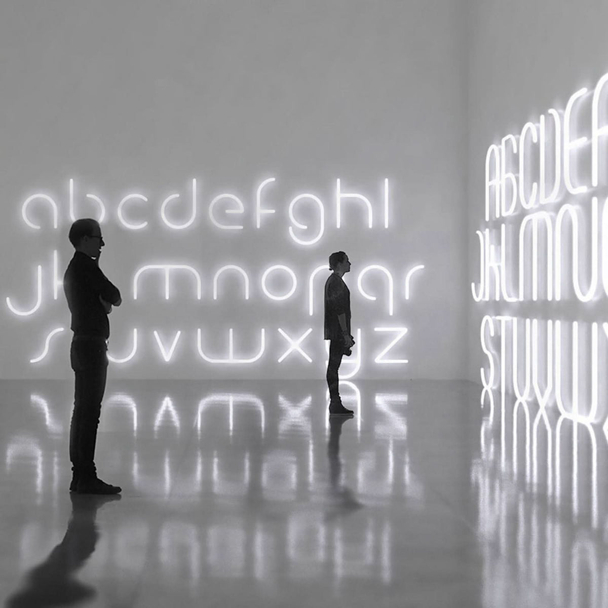 Mise en ambiance d'une installation murale avec deux silhouettes devant des lettres lumineuses.