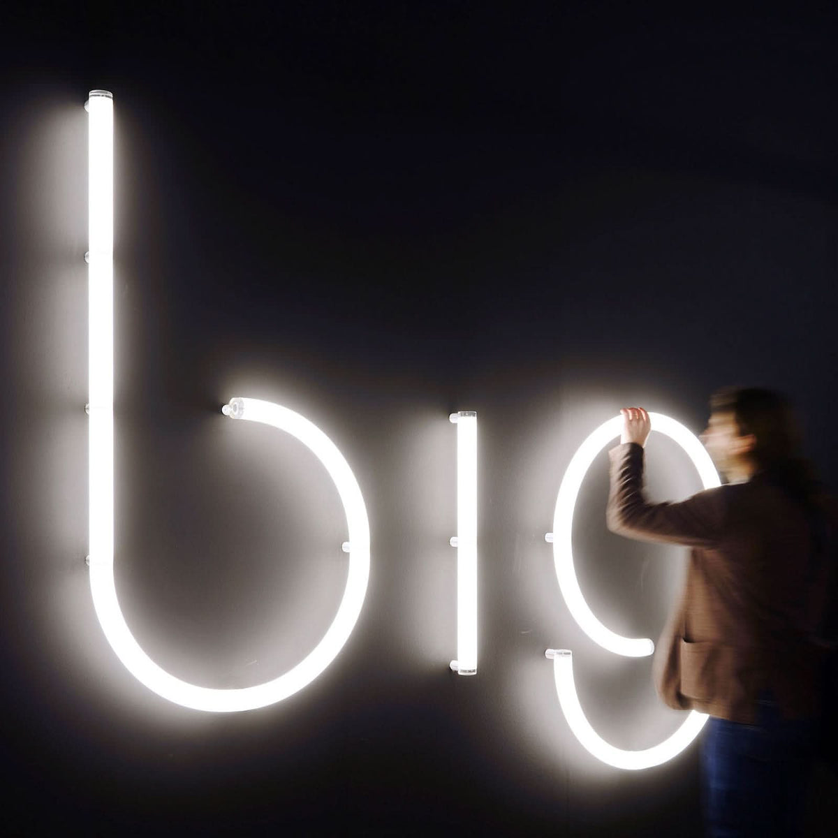 Personne en train de poser ou régler de grandes lettres lumineuses blanches sur un mur noir.