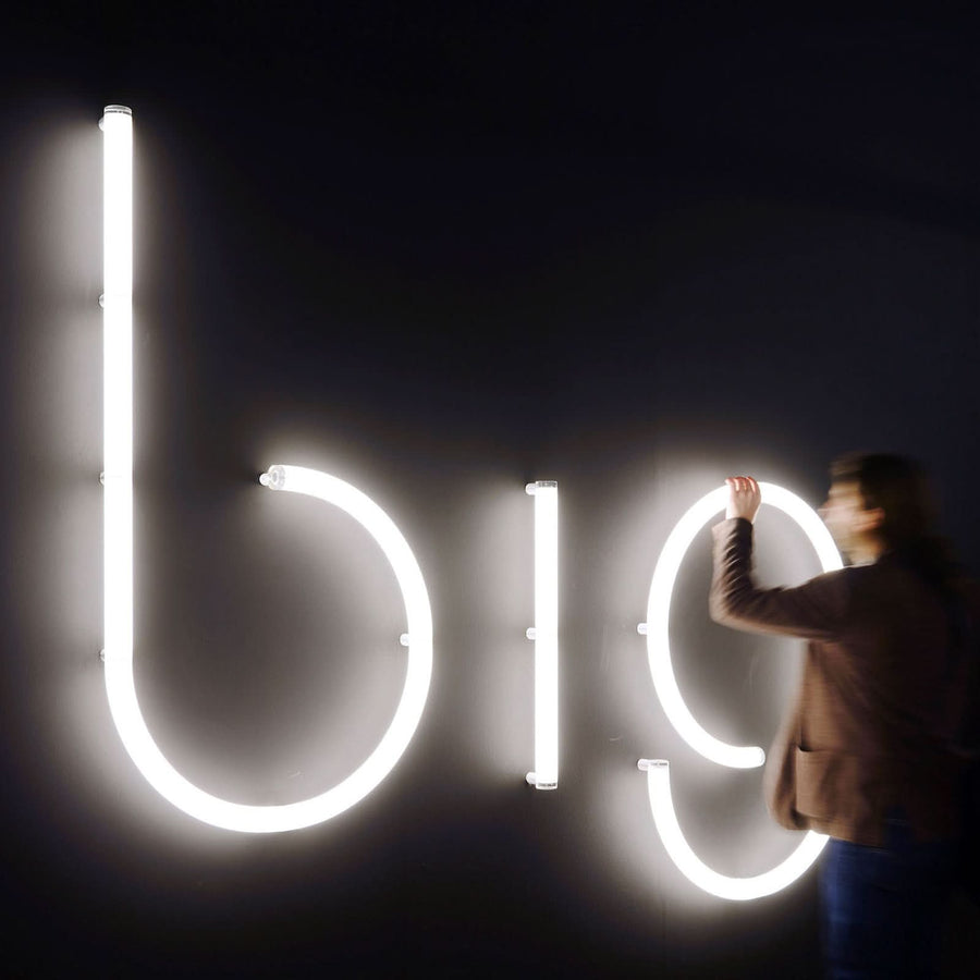 Personne en train de poser ou régler de grandes lettres lumineuses blanches sur un mur noir.