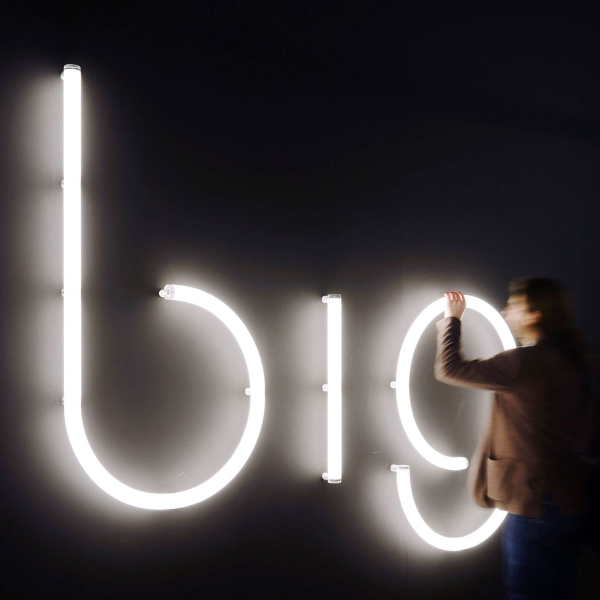 Personne installant de grandes lettres lumineuses blanches sur un mur sombre.