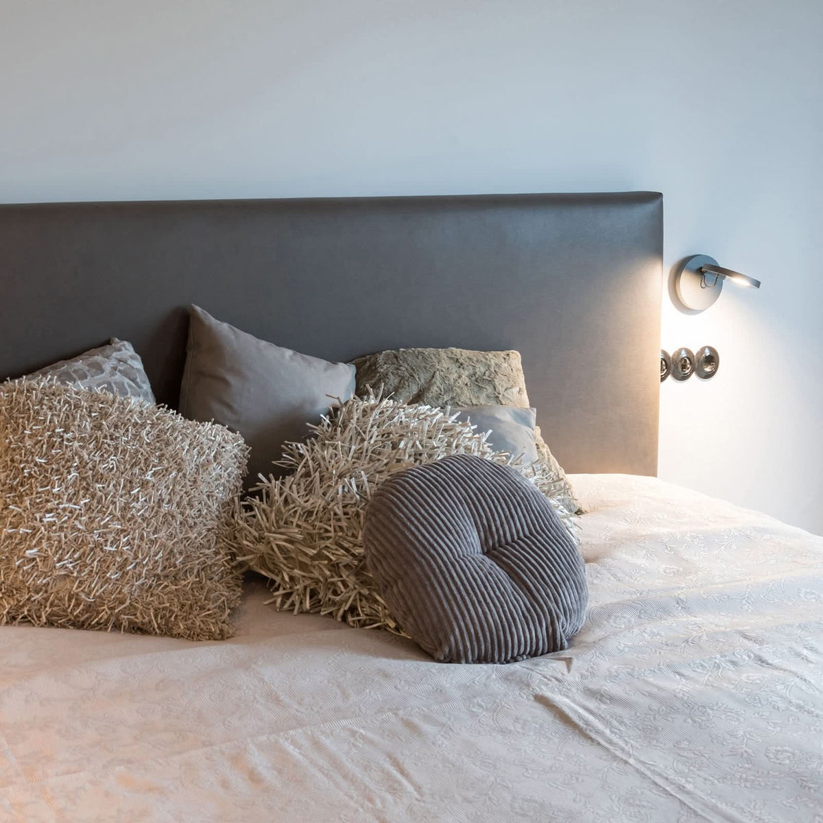 Ambiance de chambre avec l'applique murale allumée près de la tête de lit et des coussins.