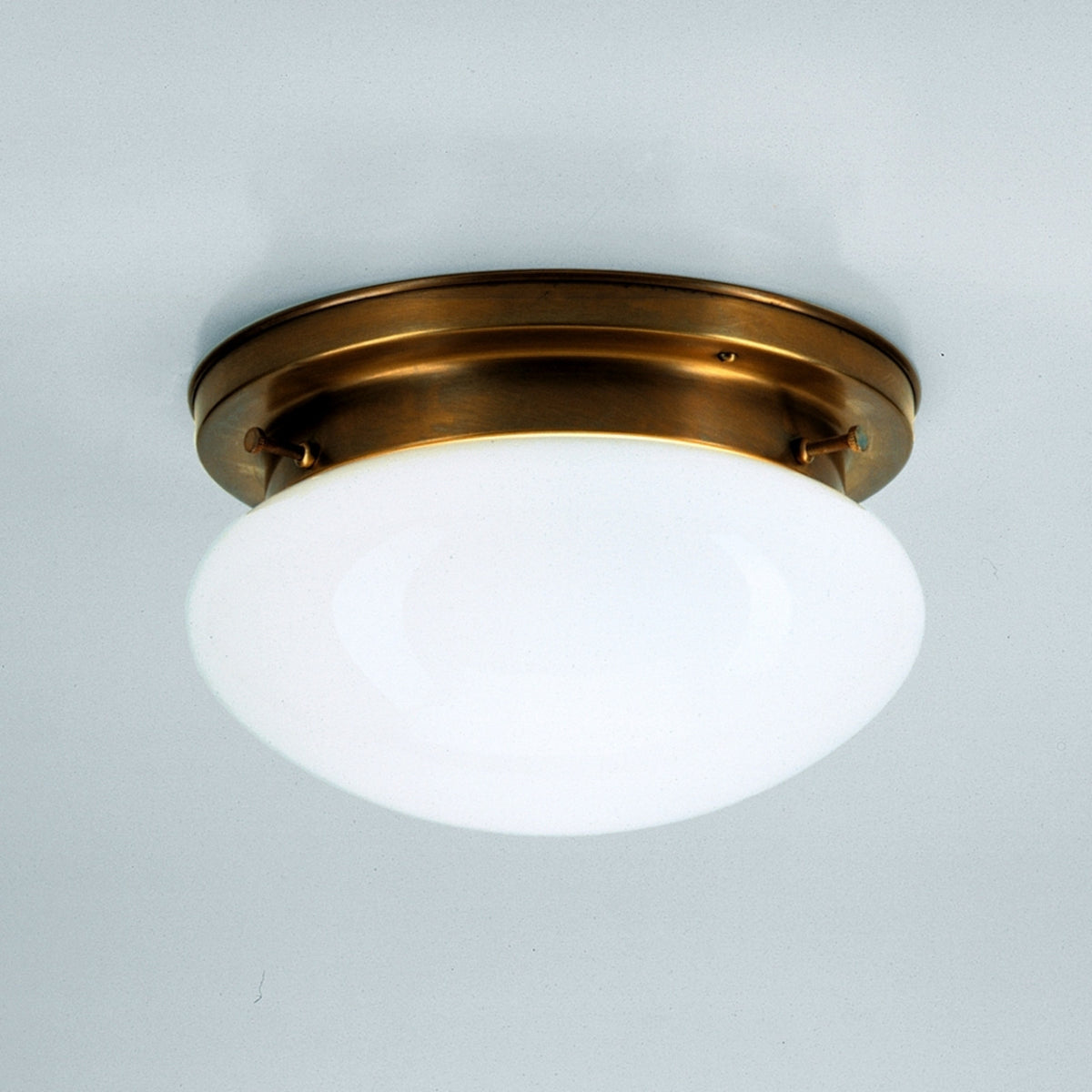 Plafonnier en laiton vieilli et globe opale fixé au plafond sur fond clair.