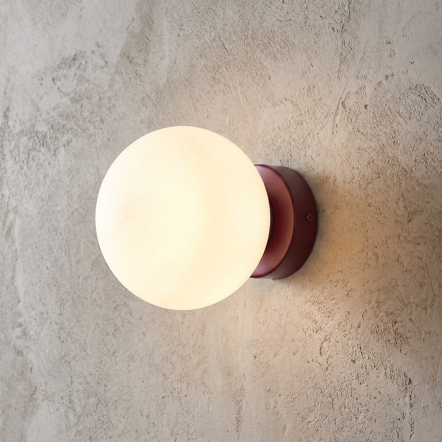 Gros plan du luminaire allumé sur un mur texturé, lumière chaude diffusée.