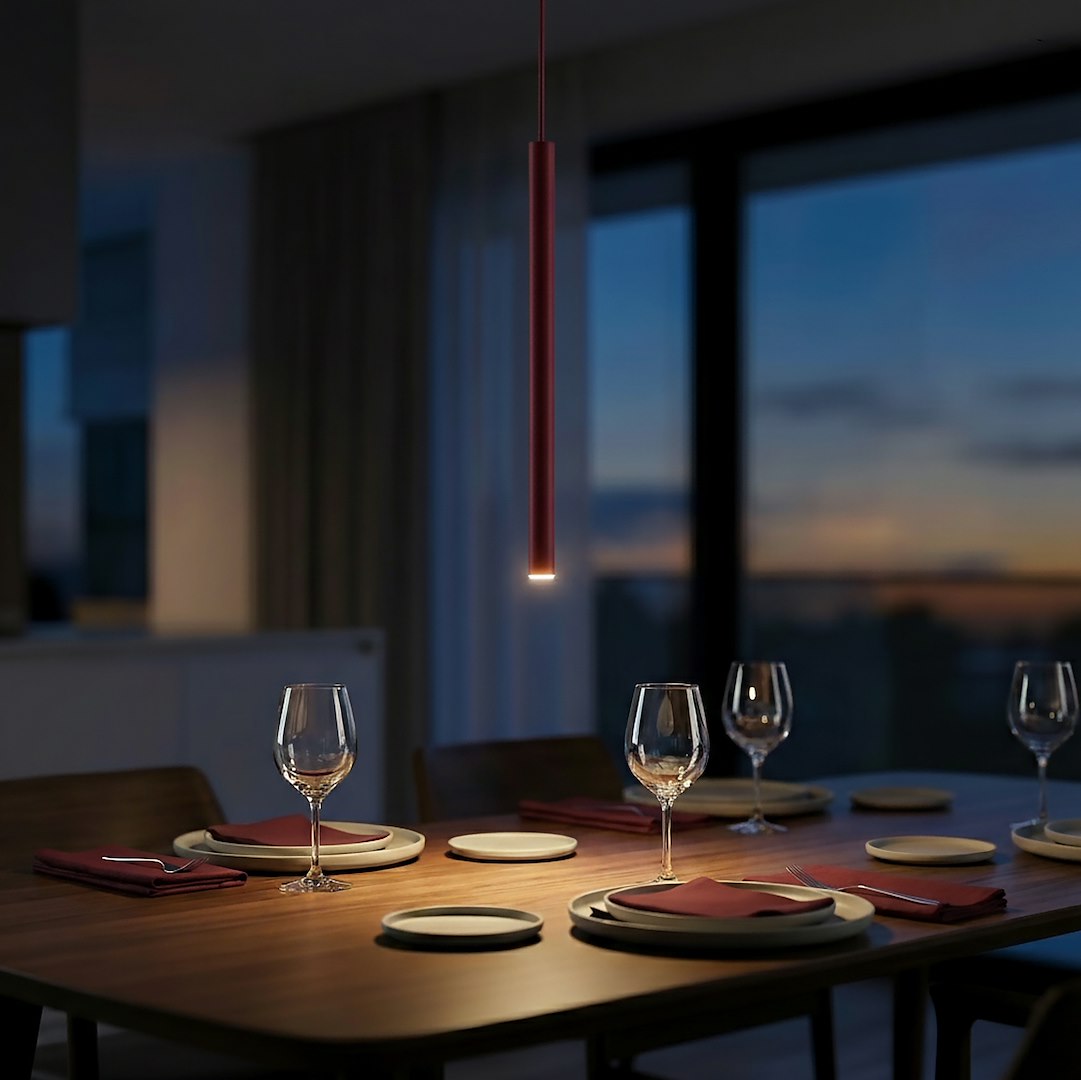 Ambiance crépusculaire, suspension allumée au-dessus d'une table dressée avec verres et baie vitrée.