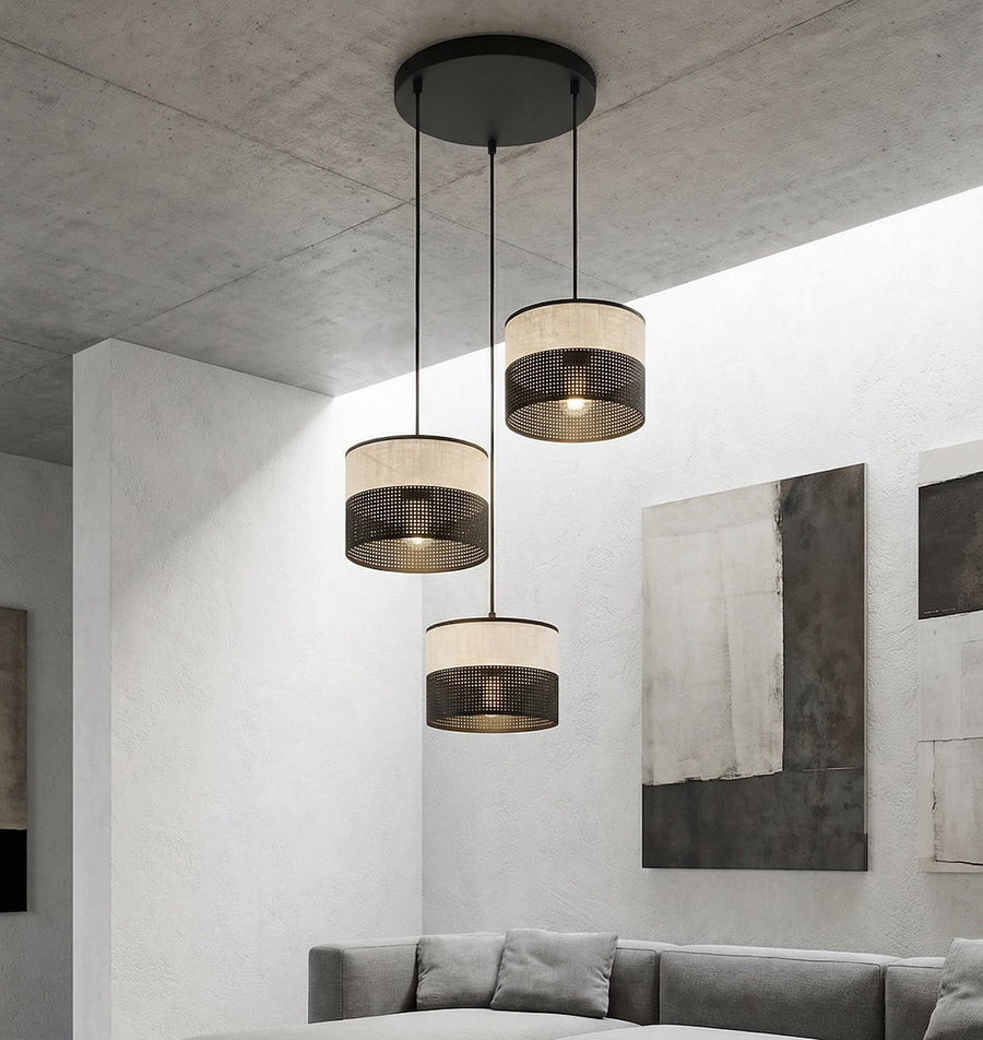 Scène de salon béton avec canapé gris et trois suspensions cylindriques allumées au plafond.