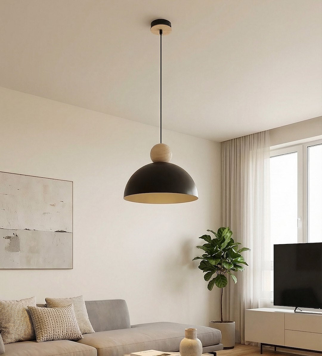 Luminaire suspendu dans un salon clair, canapé gris, plante et grande fenêtre.