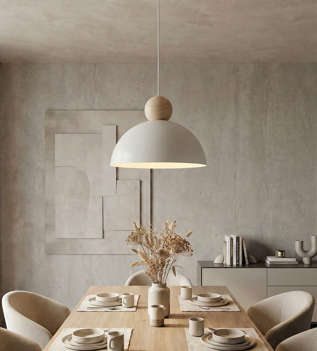 Mise en ambiance intérieure béton, luminaire éclairé au-dessus d'une table et vase séché.