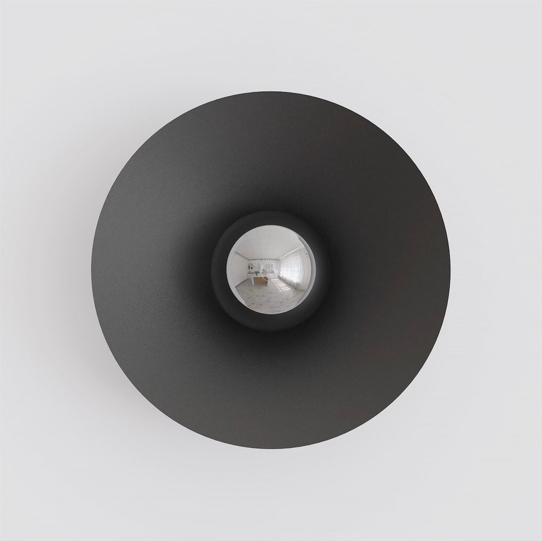 Vue de face sur fond blanc, disque noir et verre central réfléchissant une pièce.