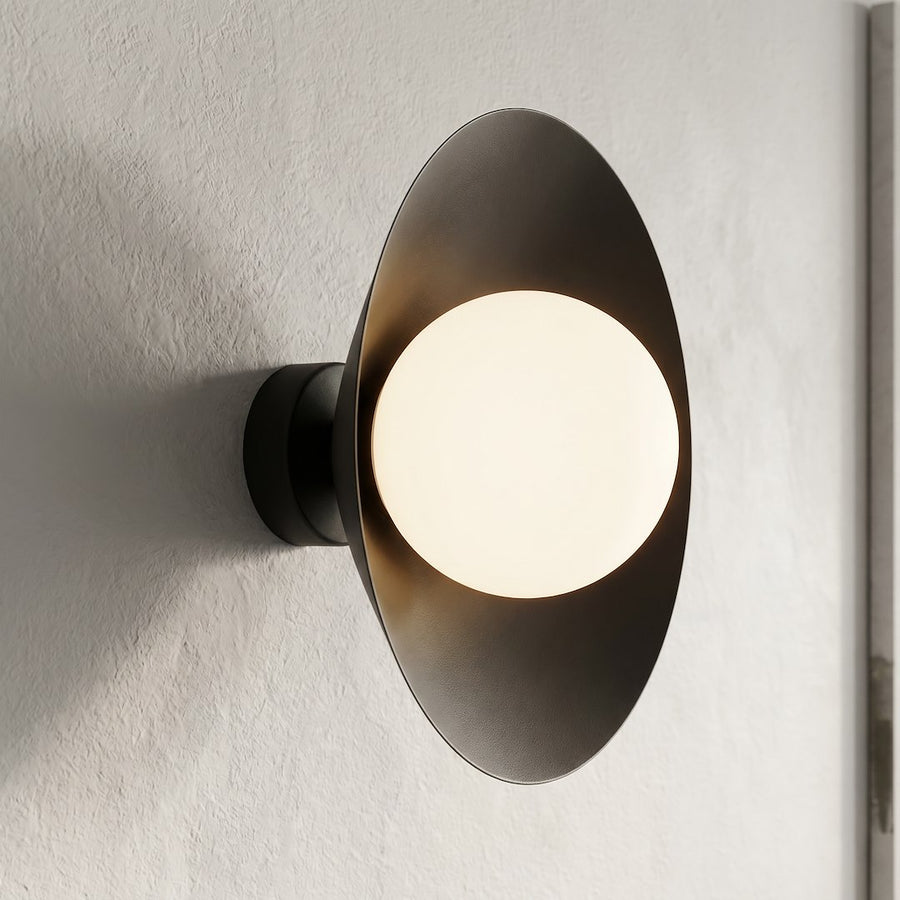 Gros plan sur mur texturé, applique murale noire allumée et diffuseur en verre blanc lumineux.