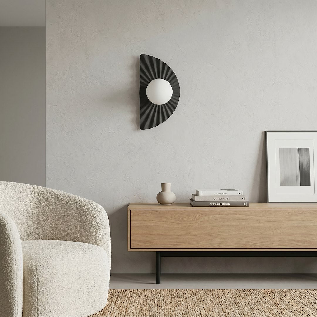 En situation dans un salon : applique murale sur mur clair, fauteuil bouclé et meuble.