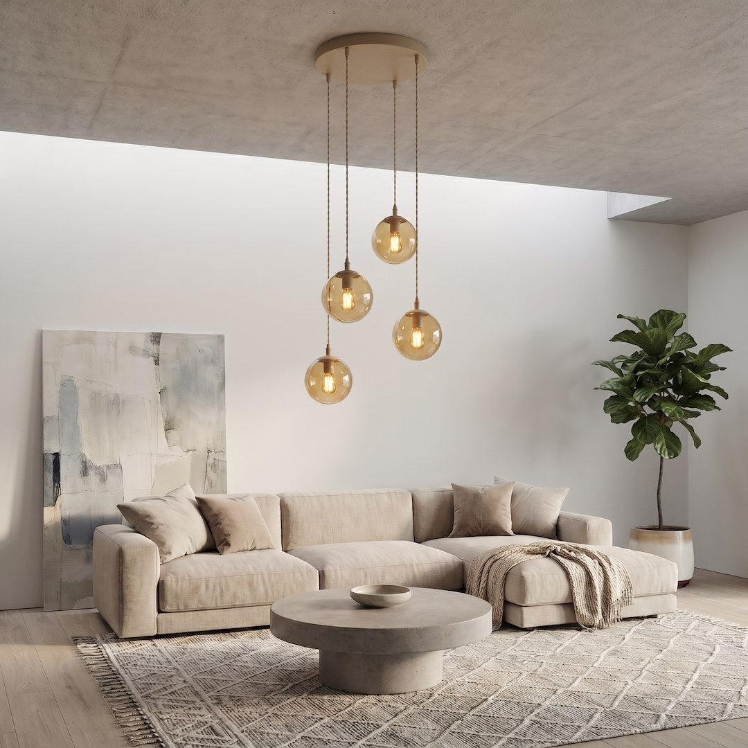 Scénographie salon clair, canapé beige et suspension dorée allumée en hauteur.