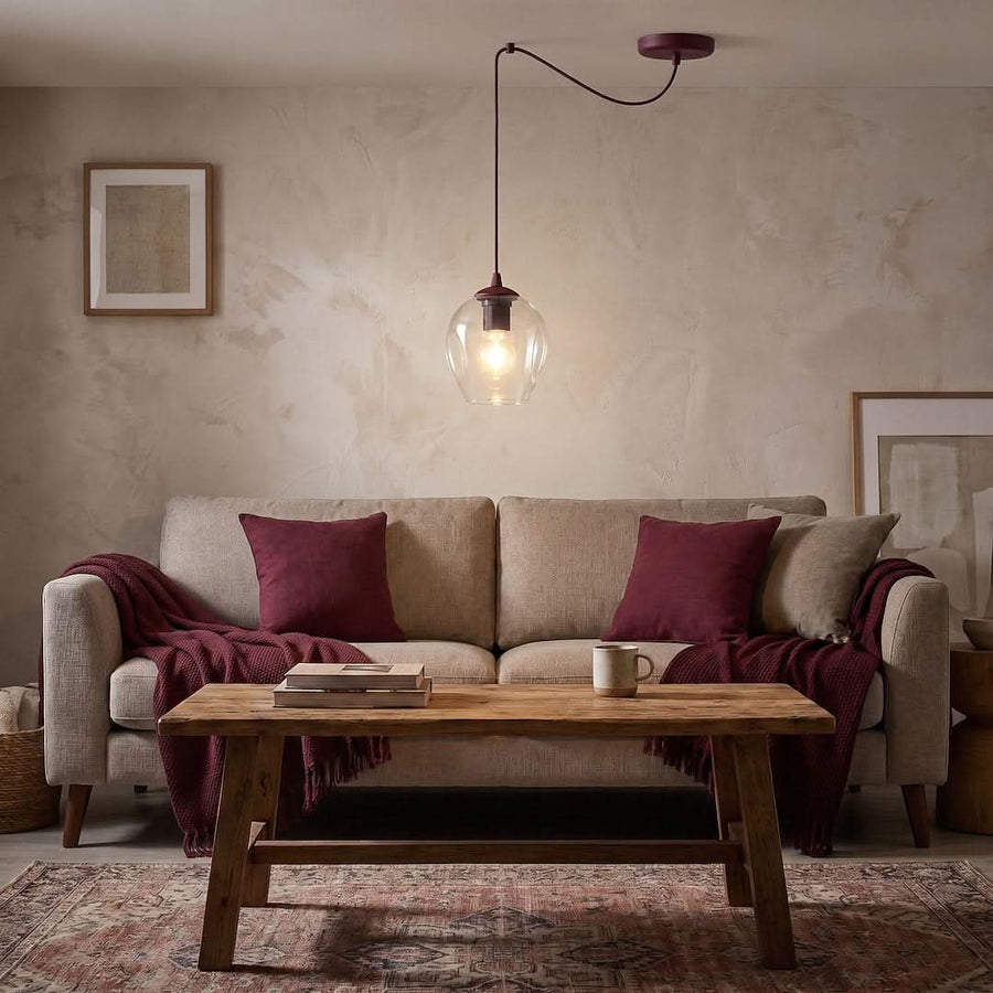 Ambiance salon cosy, canapé beige, coussins bordeaux et suspension en verre allumée