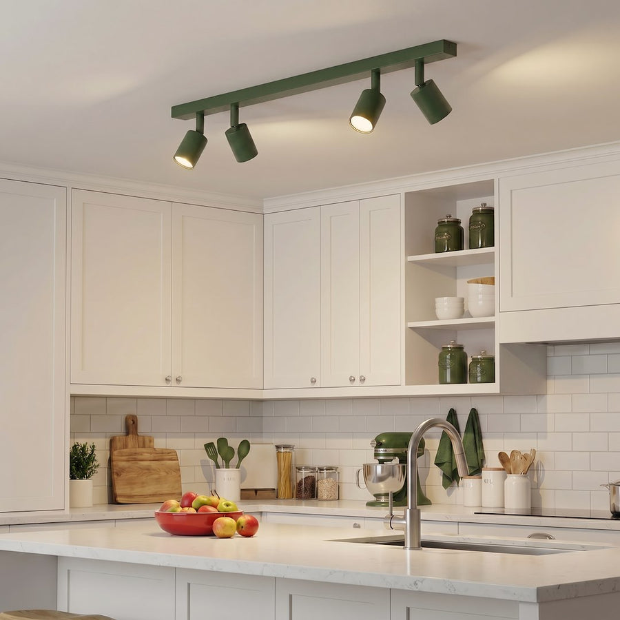 Plafonnier vert éclairant un plan de travail blanc avec pommes et accessoires verts.