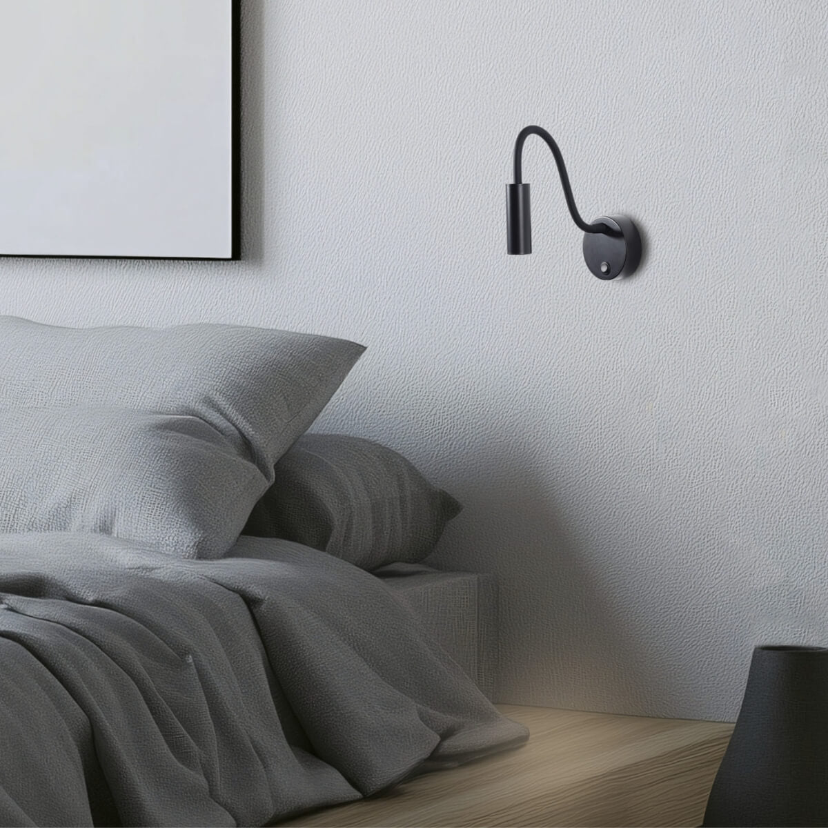 Détail de l'applique noire fixée au mur texturé, au-dessus de coussins gris dans une chambre.