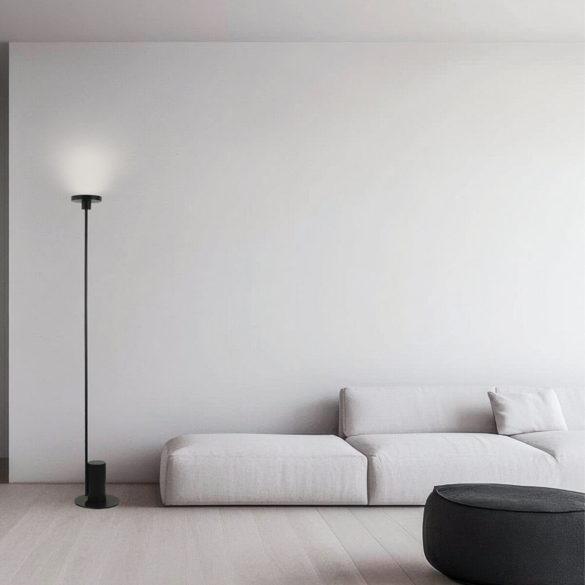 Vue large du salon épuré avec canapé modulable blanc, pouf noir et lampe
