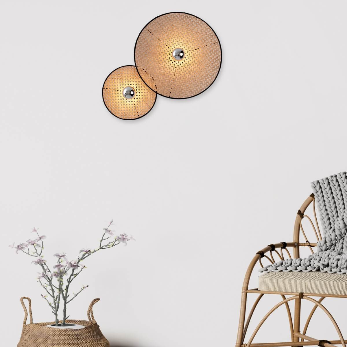 Paire d'appliques allumées sur mur clair, fauteuil rotin et plante