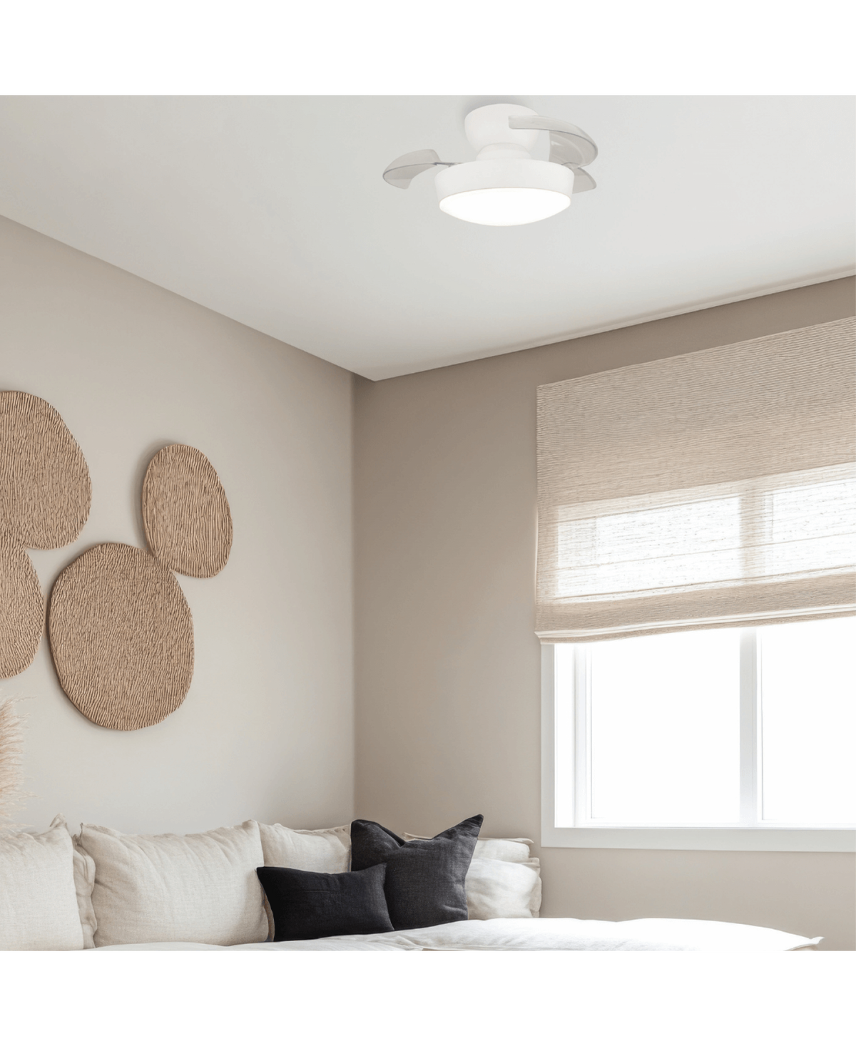 Le luminaire ventilateur blanc éclairant une chambre épurée avec lit, coussins et fenêtre.