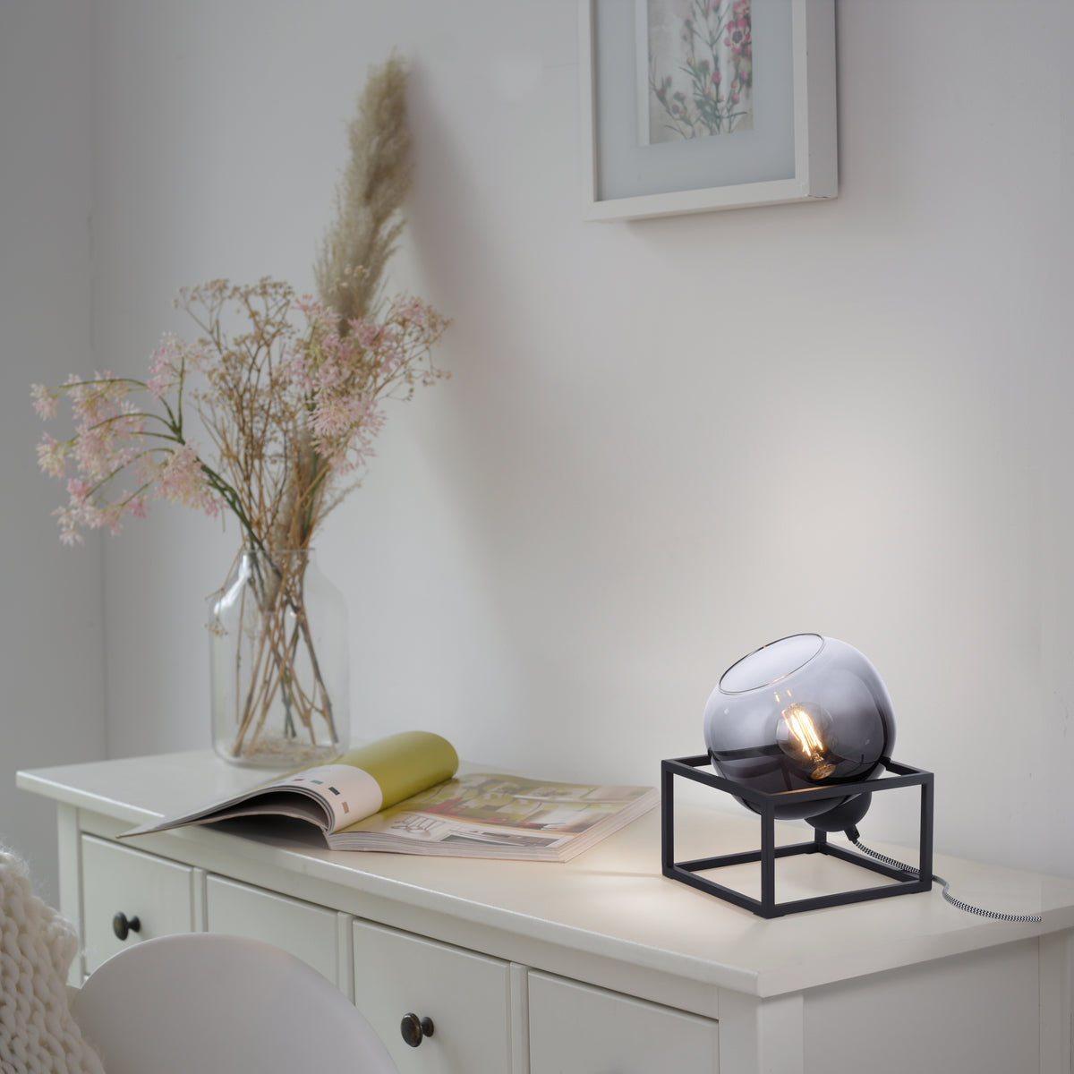 Mise en ambiance sur une commode blanche, près d'un magazine ouvert et d'un vase