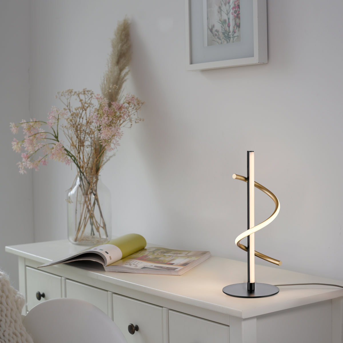 Mise en ambiance sur un meuble blanc avec vase de fleurs séchées et magazine ouvert.