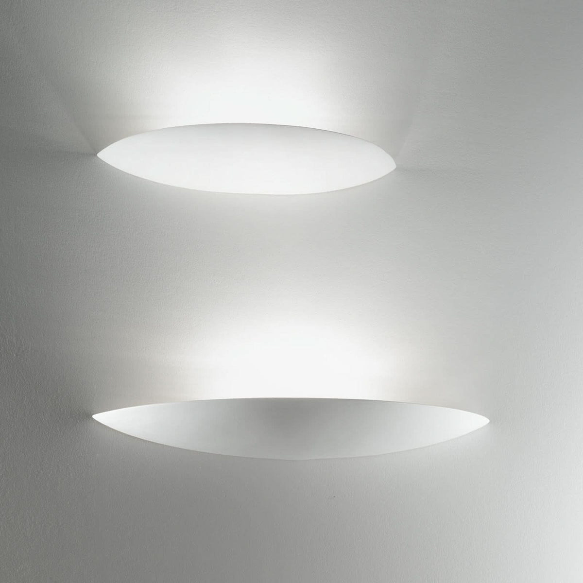 Deux appliques ovales allumées superposées sur un mur clair, halo lumineux diffus