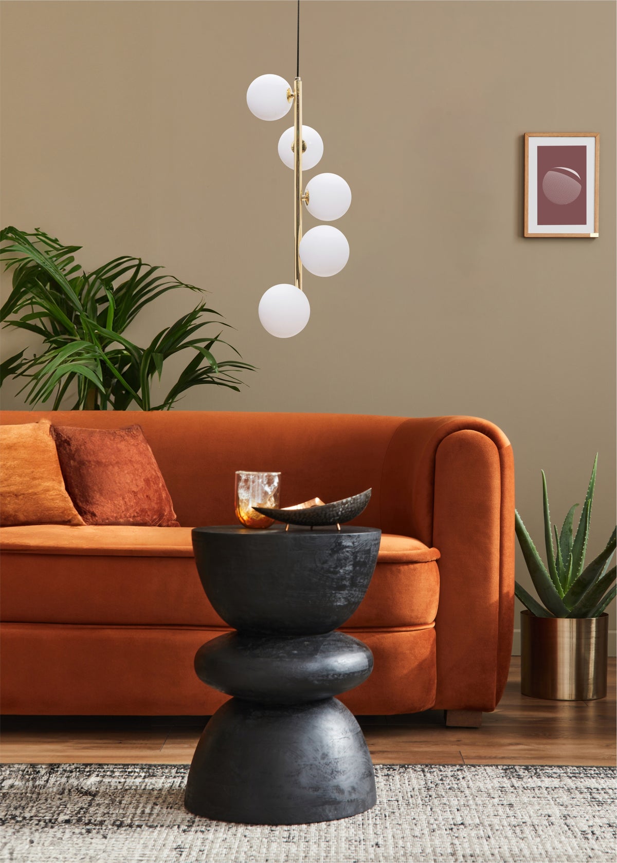 La suspension éclaire un salon avec canapé orange, plante verte et table basse noire.