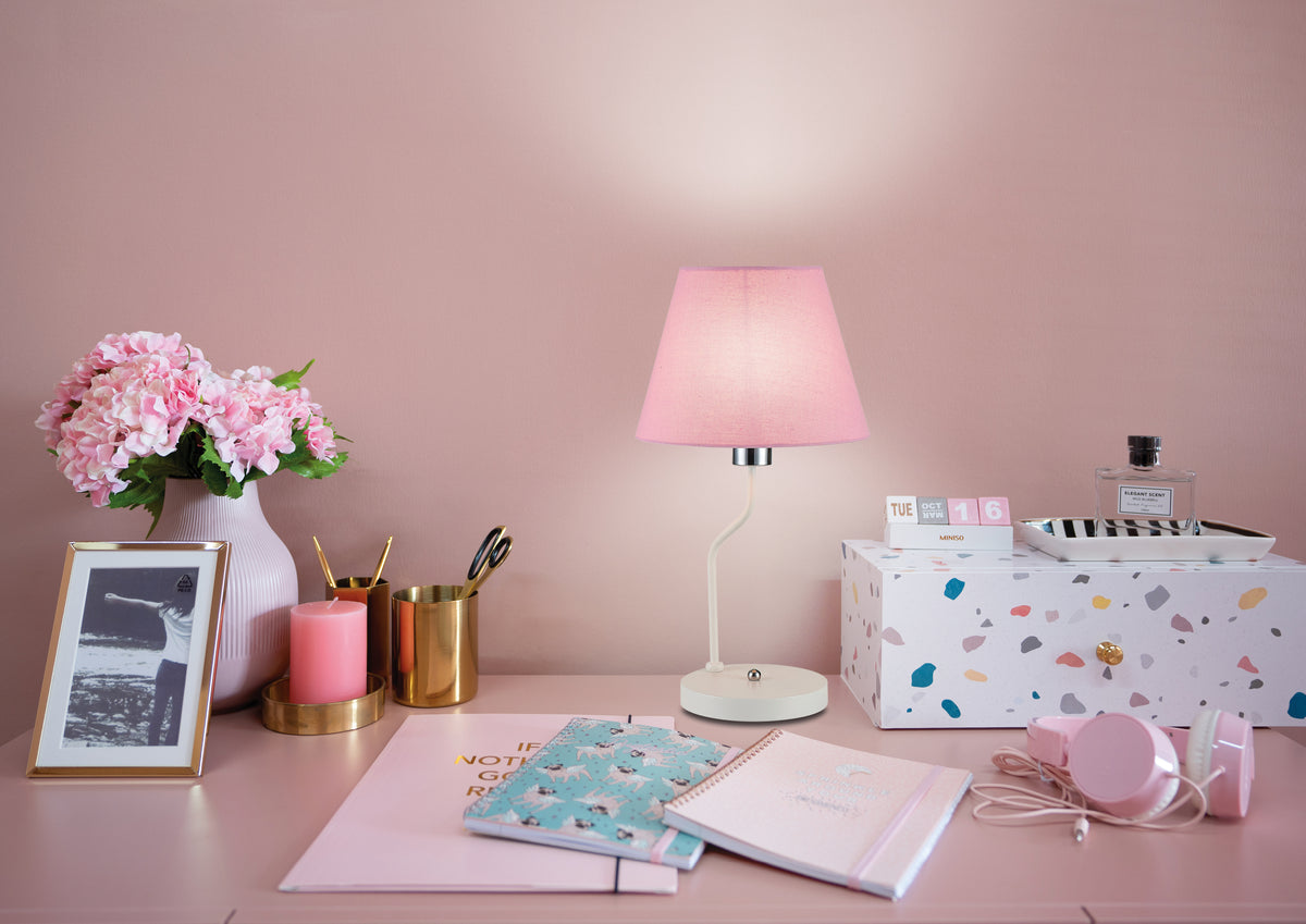 Mise en ambiance de la lampe allumée sur un bureau rose avec fleurs et accessoires