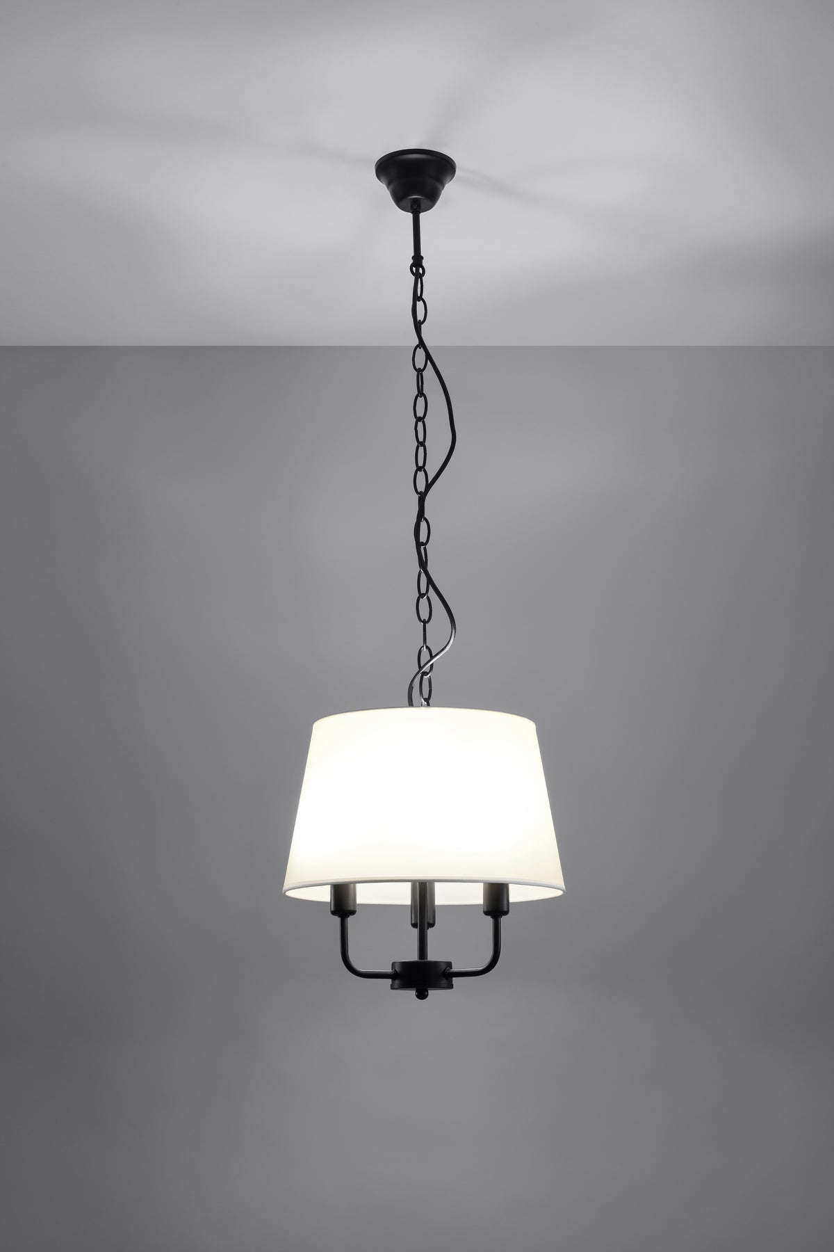 Suspension allumée sur fond gris foncé, abat-jour blanc diffusant la lumière.
