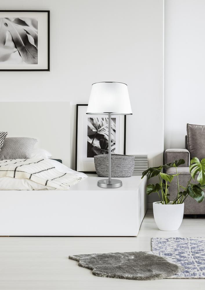 Vue de trois quarts dans une chambre, lampe allumée sur le meuble de chevet