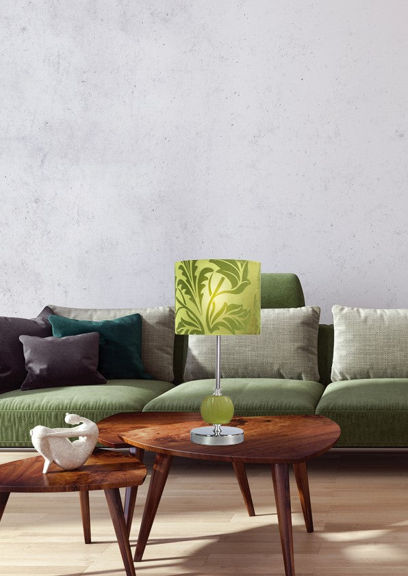 Lampe verte posée sur table basse en bois devant canapé vert et coussins