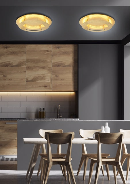 Deux plafonniers dorés allumés au plafond d'une cuisine moderne avec meubles en bois.