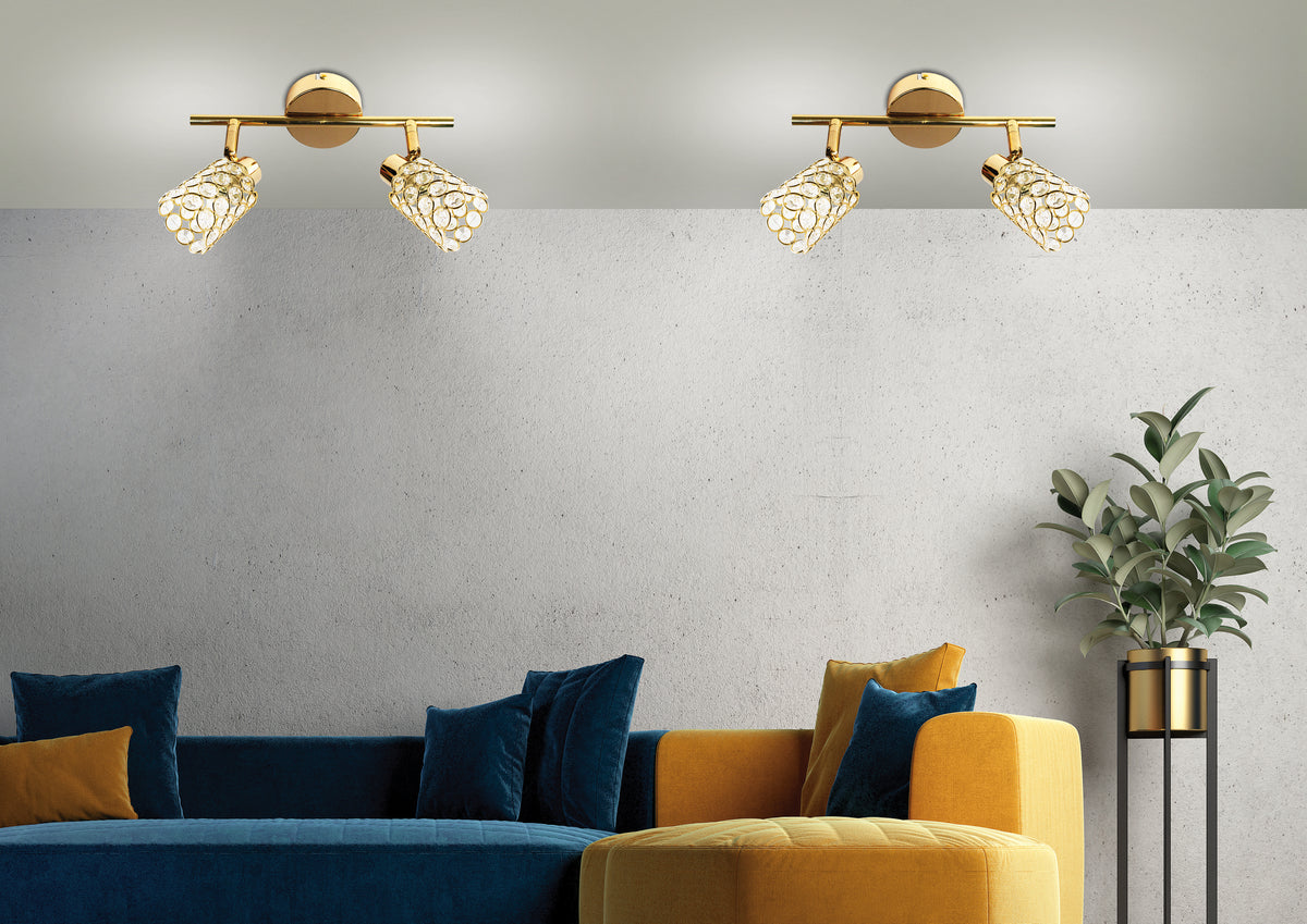 Mise en ambiance de deux plafonniers allumés au-dessus d'un canapé bleu et moutarde sur mur béton.
