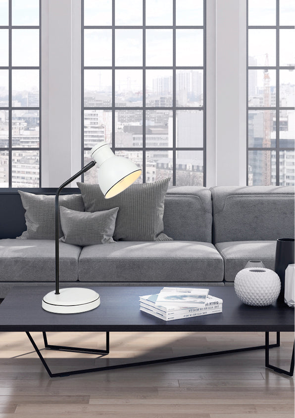 Lampe allumée sur table basse devant canapé gris et fenêtres urbaines