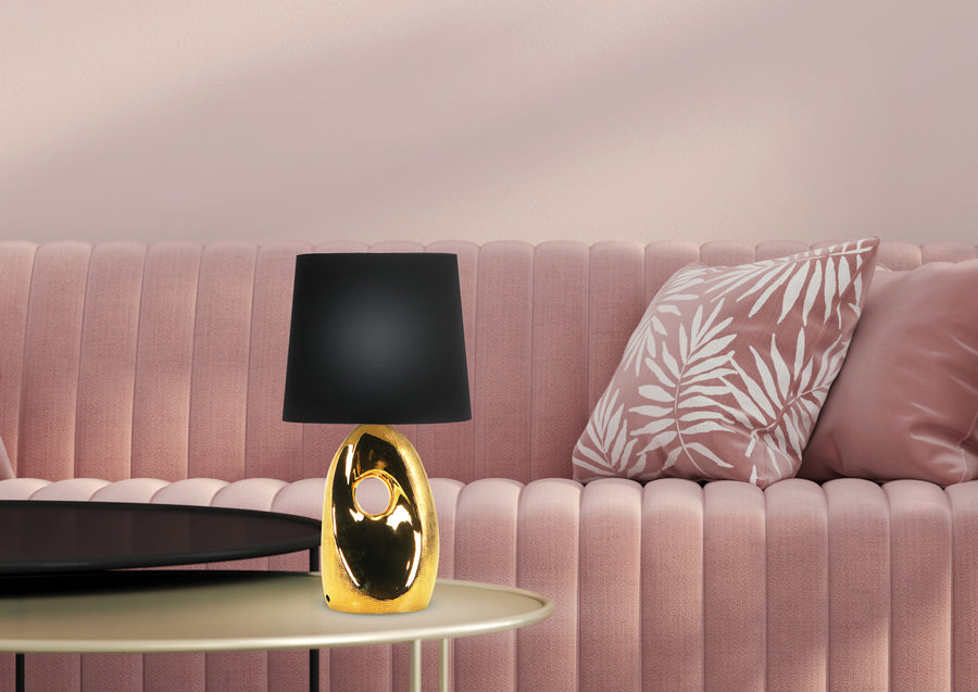 Ambiance salon rose, lampe dorée à abat-jour noir posée sur table basse