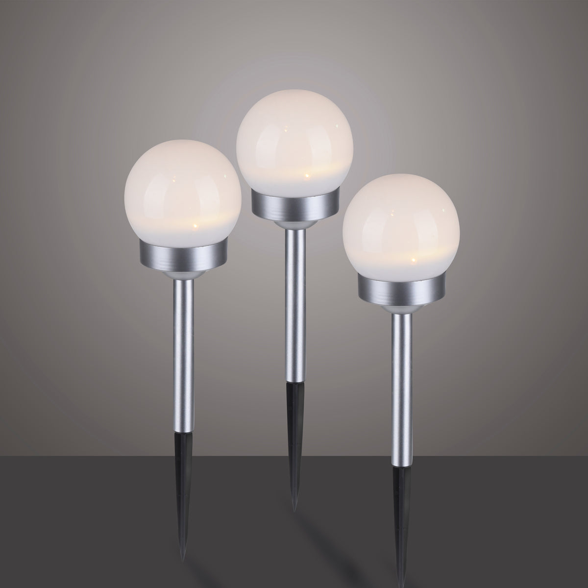 Trois globes lumineux allumés sur tiges acier et pointes noires, présentation studio centrée