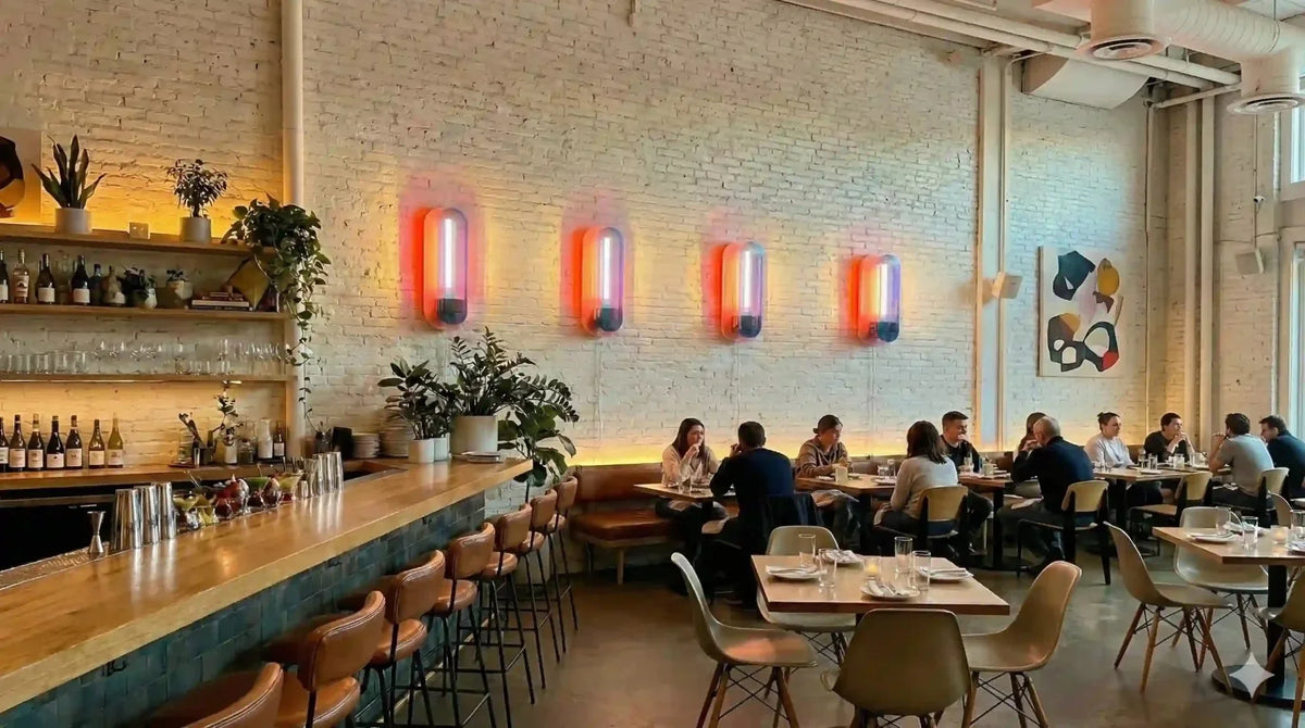 Quatre appliques roses alignées au-dessus du bar d'un restaurant animé