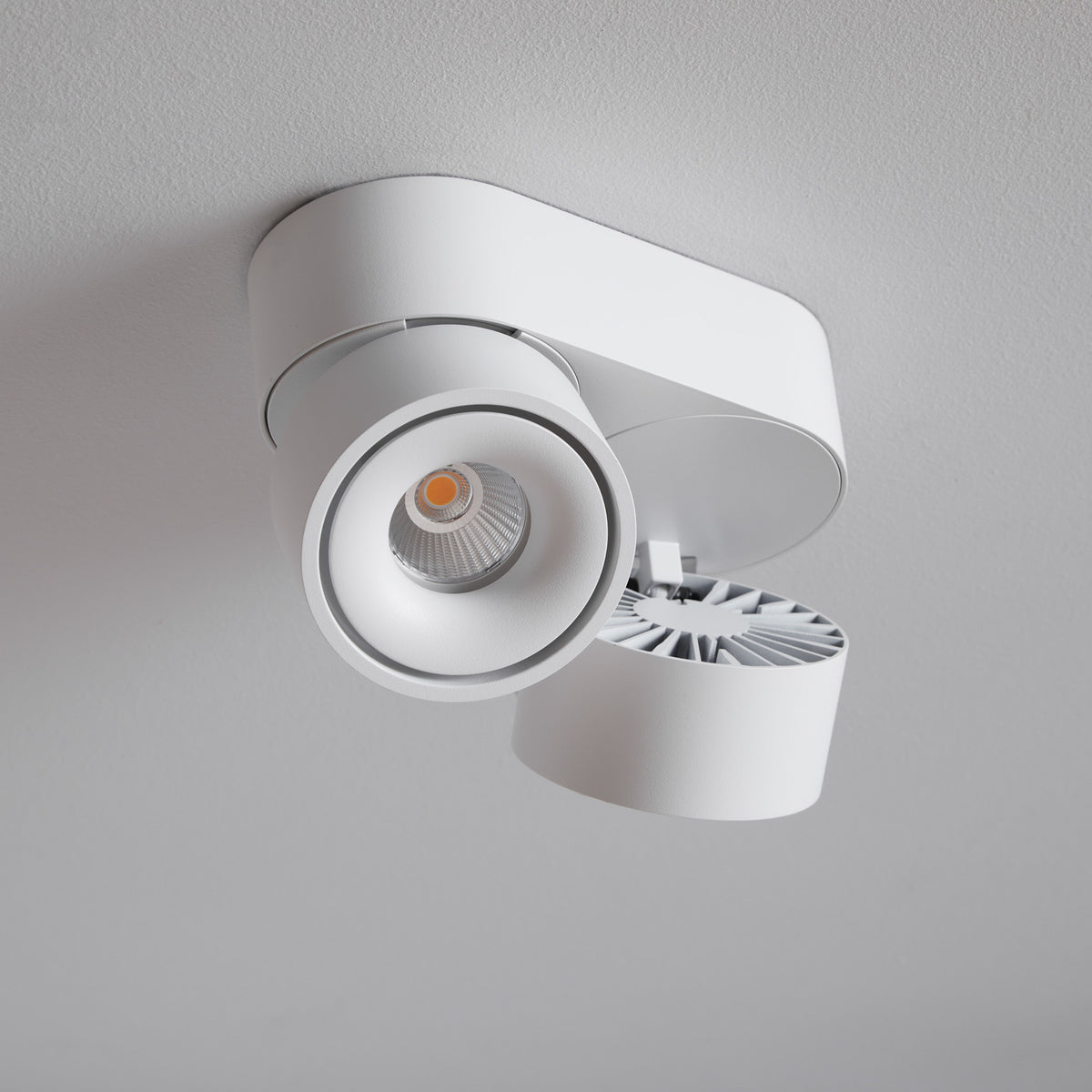 Vue rapprochée du spot blanc monté au plafond, montrant ses deux projecteurs orientables.